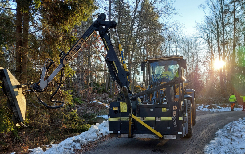 Hjullastare med sågklingor klipper ner växtlighet längs enskild väg.