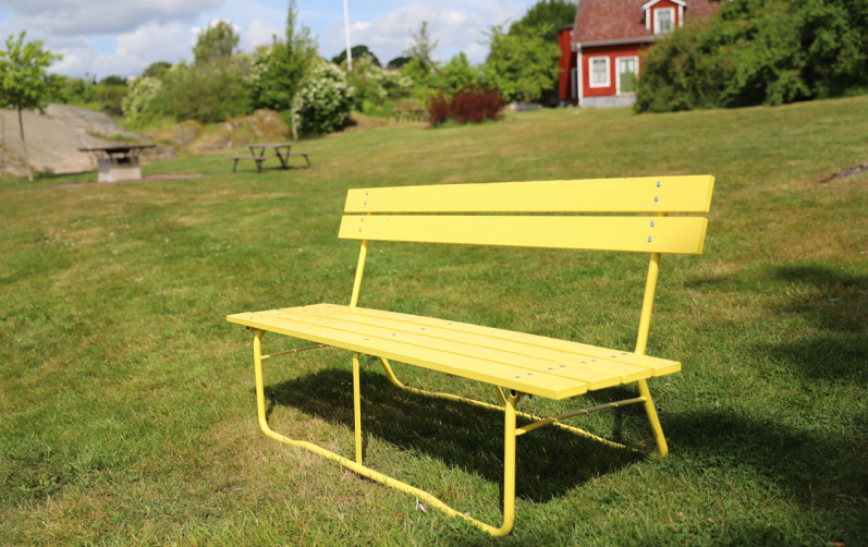 Gul parkbänk i parkmiljö.