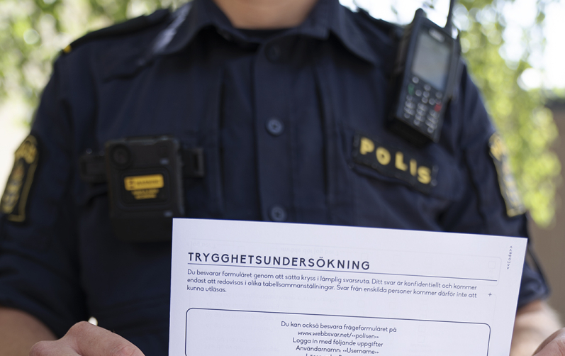 Person i polisuniform håller upp ett papper med enkätfrågor framför sig.
